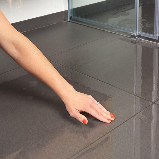 Hand van vrouw met oranje nagellak veegt over natte, glanzende donkergrijze vloertegels bij een douchecabine.