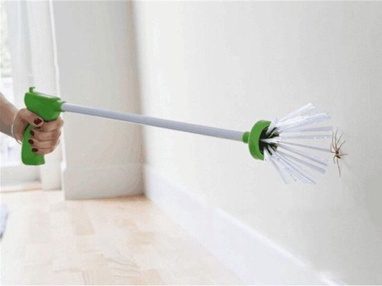 Een persoon vangt een spin op een witte muur met een groene spinnenvanger.