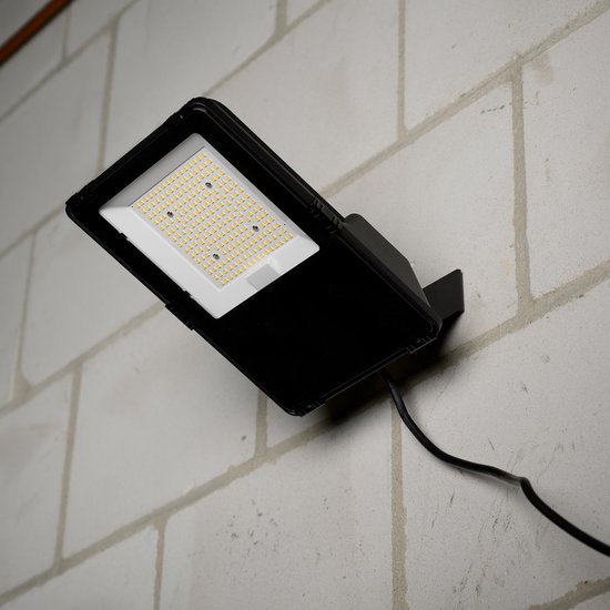 Zwarte LED-schijnwerper met LED's aan, gemonteerd op een bakstenen muur.