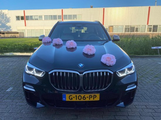 Zwarte BMW met vier lichtroze bloemstukken op de motorkap.
