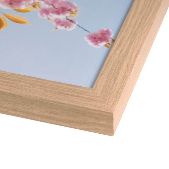Een close-up van een houten fotolijst met een lichtgekleurde essenhout finish, met op de achtergrond een deel van een print van roze bloesems.