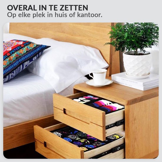 Houten nachtkastje met twee open lades, gevuld met gekleurd ondergoed en sokken, naast een bed met witte lakens en een sierkussen.
