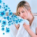 Femme aux yeux fermés sentant un vêtement blanc, entourée de fleurs bleues. Machine à laver en arrière-plan.
