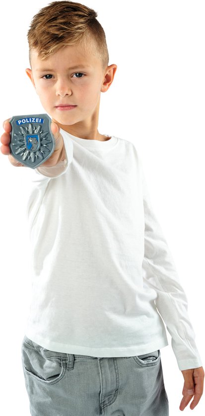 Jongen in wit shirt en grijze jeans houdt een politiebadge omhoog.