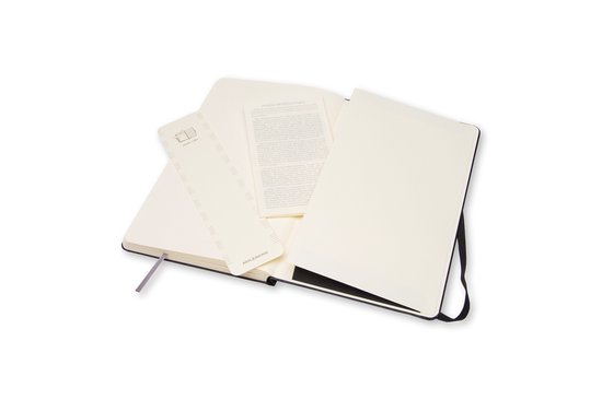 Open zwart Moleskine notitieboek met een muziekliniaal, een vouwblaadje en een blanco pagina.