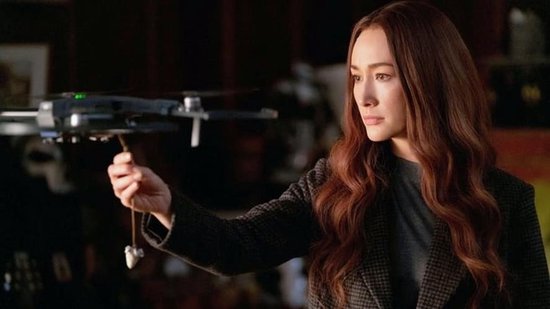 Maggie Q met lang bruin haar, houdt een drone vast.