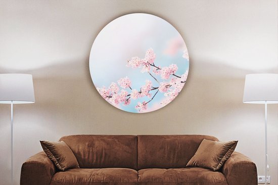 Cercle mural rond avec des branches de fleurs roses au-dessus d'un canapé marron avec coussins, flanqué de lampadaires.