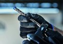 Handen met zwarte werkhandschoenen die een SDS plus-7X boor in een boormachine plaatsen
