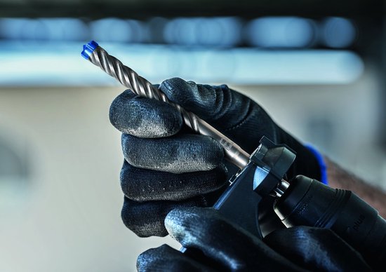 Handen met zwarte werkhandschoenen die een SDS plus-7X boor in een boormachine plaatsen