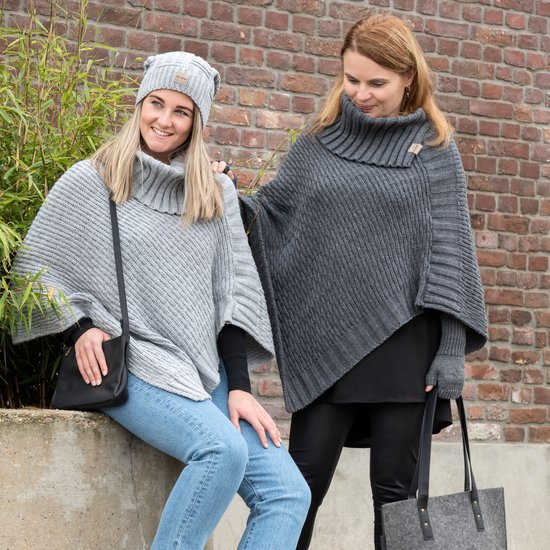 Twee vrouwen, één in grijze poncho en muts, ander in donkergrijze poncho met hoge kraag. Zwarte tas en handtas.