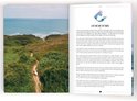 Een kustlandschap met groene heuvels en de oceaan, met twee wandelaars op een pad.