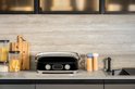 Zwarte contactgrill met chromen handgreep, gesloten, op een aanrecht.