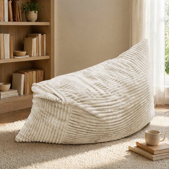 Crèmekleurige zitzak met ribbelstof, in een woonkamer bij een boekenplank.