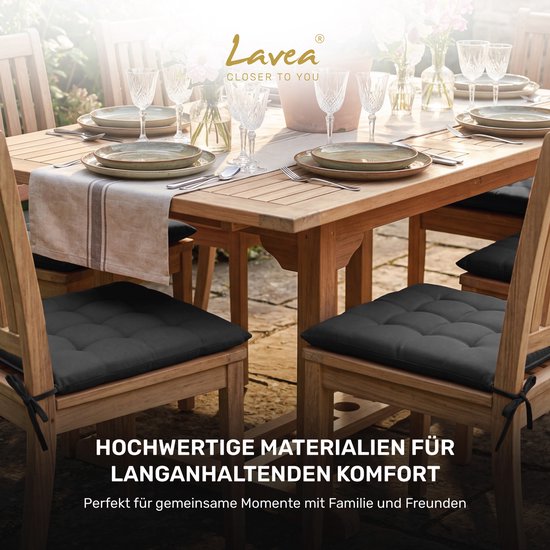 Donkergrijze zitkussens op houten stoelen aan een buitentafel.