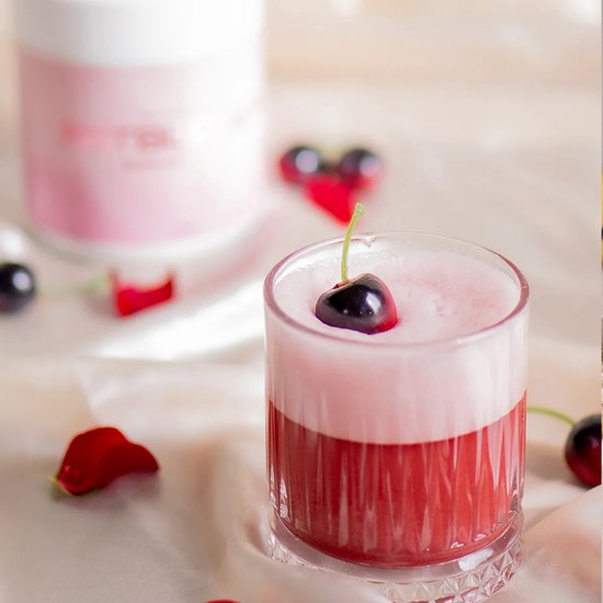 Een glas met rode drank, roze schuim en een kers als garnering. Een pot met "FATBURNER" staat op de achtergrond.