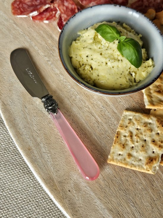 Botermesje met roze handvat, zilverkleurig metaal en versiering. Naast een kom met boter en crackers.