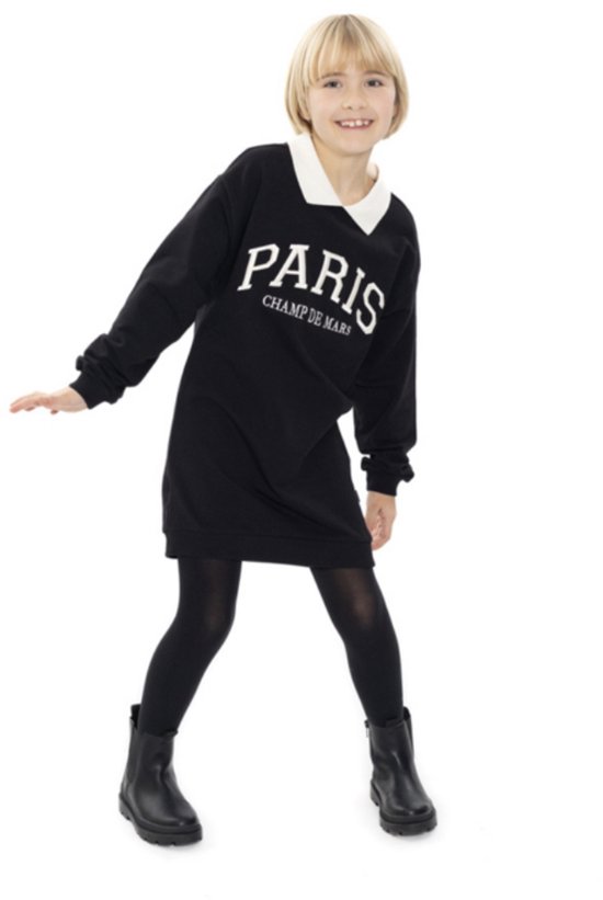 Meisje in zwart jurkje met witte kraag en 'PARIS CHAMP DE MARS' opdruk, met zwarte panty en laarsjes.