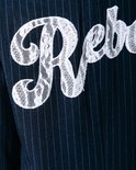 Detail van de witte kanten applicatie 'Rebels' op een donkerblauw pinstripe colbert.