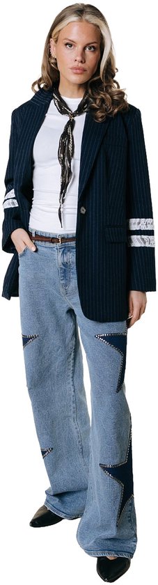 Vrouw met blond haar, draagt donkerblauw pinstripe colbert met kanten details, wit T-shirt en lichte jeans met sterren.