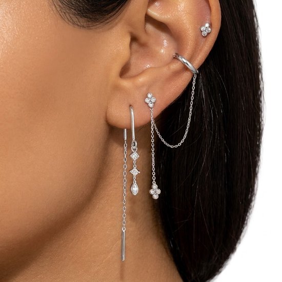 Modèle portant des clous d'oreilles argentés à détails floraux, un grimpeur d'oreille à chaînette et une longue boucle d'oreille à trois pendentifs: fleur, goutte, barre.