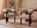 Twee beige bouclé stoelen met gebogen rugleuning en zwarte poten in een sfeervolle setting.
