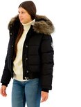 Model met een zwarte Superdry bomberjack met dikke bontkraag, witte coltrui en spijkerbroek.