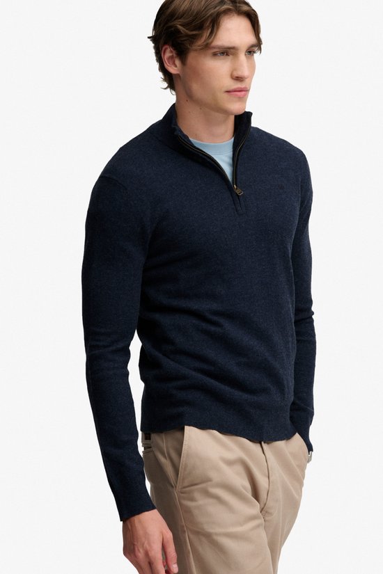 Man met donkerblauwe melange trui met ritssluiting, lichtblauw T-shirt en beige broek.