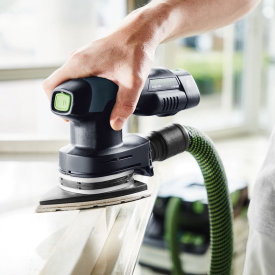 Een hand schuurt een witte rand met een zwarte schuurmachine met groen accent en een groen gestreepte slang.