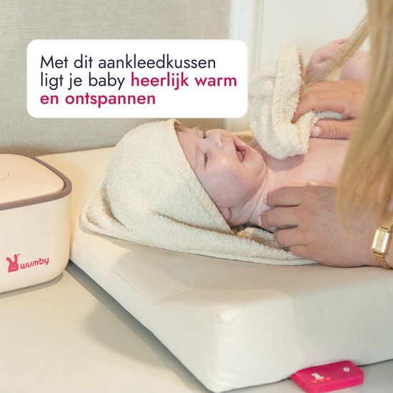 Een baby met een handdoek om het hoofdje ligt op een zandkleurig aankleedkussen.