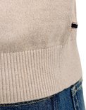 Onderlichaam van een man in een lichtbeige gebreid poloshirt met lange mouwen en geribde zoom, met een donkerblauwe jeans.