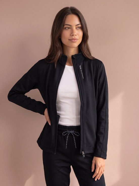 Model draagt een open zwart sportvest met witte top en zwarte sportbroek met witte veters.
