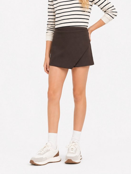 Model in een donkerbruine skort met wikkeleffect, gestreepte top, witte sokken en sneakers.