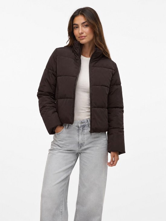 Vrouw met een bruine, korte, gewatteerde jas met opstaande kraag en ritssluiting, gedragen over een witte top en lichte jeans.