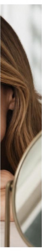 Zijprofiel van een vrouw met golvend bruin haar en een gouden spiegel.