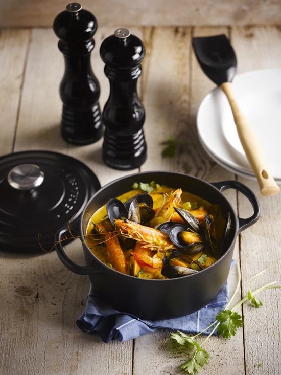 Zwarte braadpan met mosselen, garnalen en koriander op een blauwe doek.