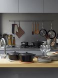 Zwarte Le Creuset braadapannen op een houten aanrecht met keukengerei.