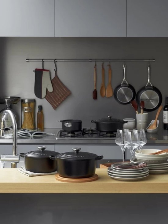 Zwarte Le Creuset braadapannen op een houten aanrecht met keukengerei.