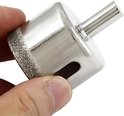 Hand houdt een zilverkleurige diamantboor met diamantbezaagde rand vast.