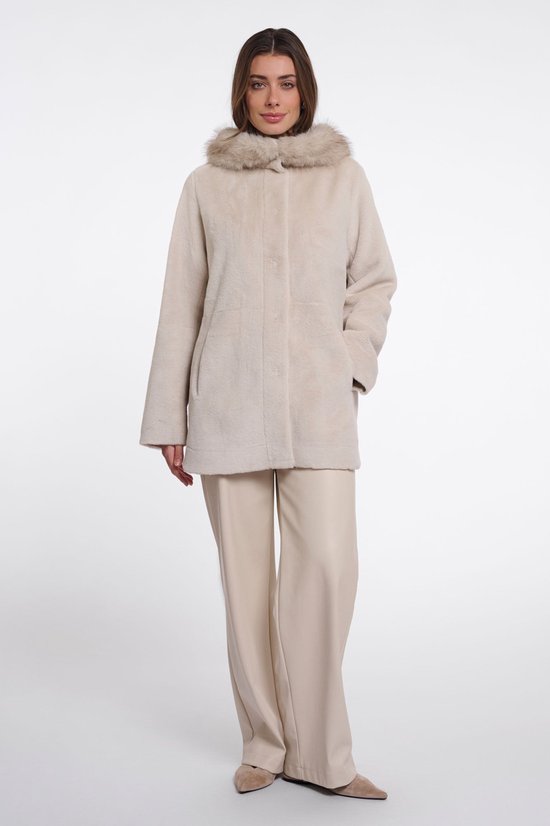 Een vrouw met bruin haar draagt een crèmekleurige jas met bontkraag en een broek.
