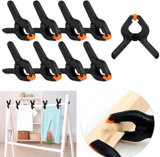Zes zwarte veerklemmen met oranje uiteinden, en een losse klem. Ook te zien: kleding aan een rek, vastgezet met klemmen, en een klem op hout.