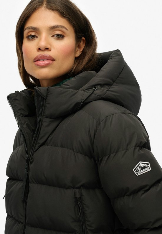 Close-up van een zwarte pufferjas met capuchon en Superdry logo op de mouw.
