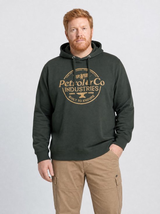 Man met rode baard in een donkergroene hoodie met goudkleurige merkprint op de borst.