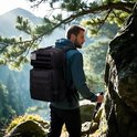 Man met zwarte tactische rugzak met Amerikaanse vlag patch, wandelend op een bergpad.
