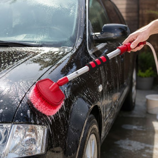 Een hand gebruikt een Dirt Devil autowasborstel om een natte, zwarte auto te wassen.