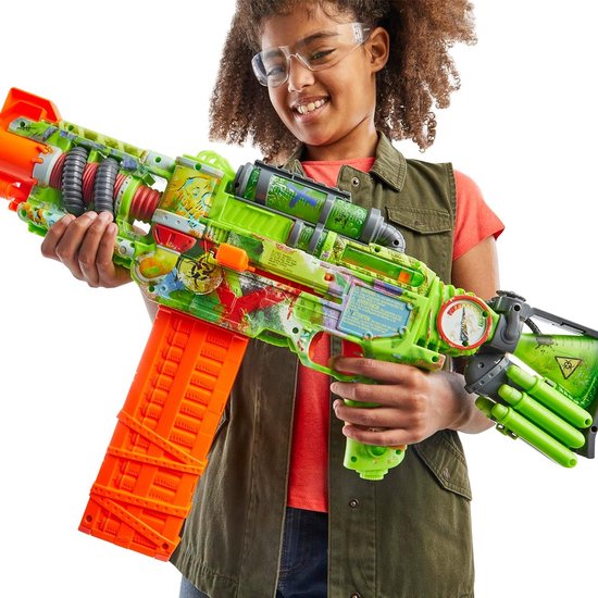 Meisje met beschermende bril houdt een grote felgroene Nerf Zombie Corrupter blaster met oranje magazijn vast, lachend.