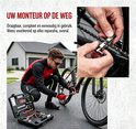 Een man in sportkleding repareert een fietsketting met een gereedschap uit de open zwarte gereedschapskist. Close-up van de kettingreparatie. Tekst: UW MONTEUR OP DE WEG.