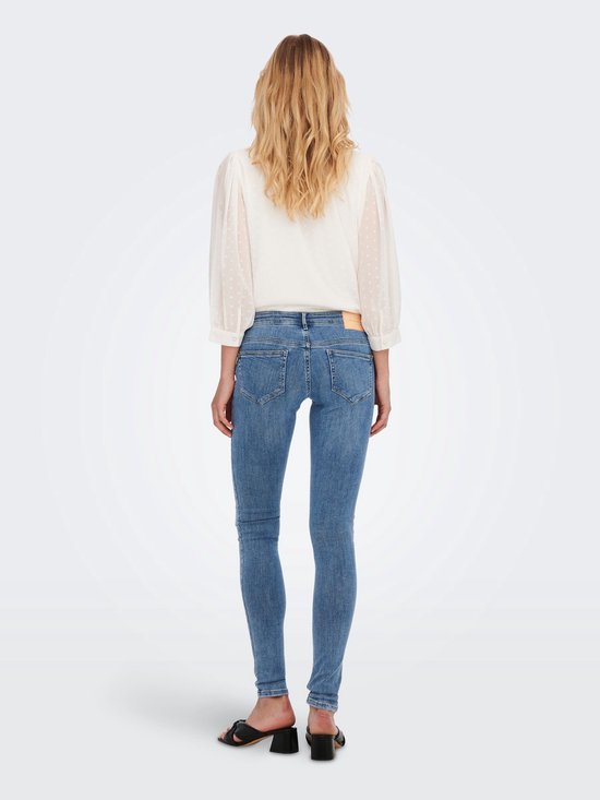 Vrouw met lang blond haar, draagt een witte blouse en lichtblauwe skinny jeans, zicht van achteren.