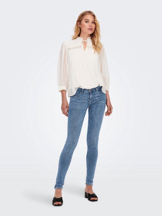 Vrouw met lang blond haar, draagt een witte blouse en lichtblauwe skinny jeans, zicht van voren.