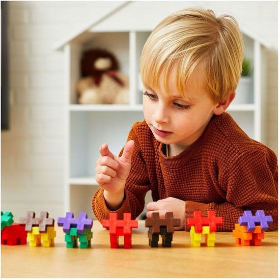 Een jongen met blond haar kijkt geconcentreerd naar kleine Plus-Plus bouwwerken op een tafel.