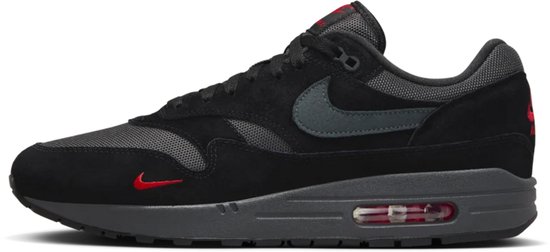 Zwarte Nike Air Max 1 sneaker met suède overlays, grijze mesh, een donkergrijze swoosh en rode Nike-logo's.